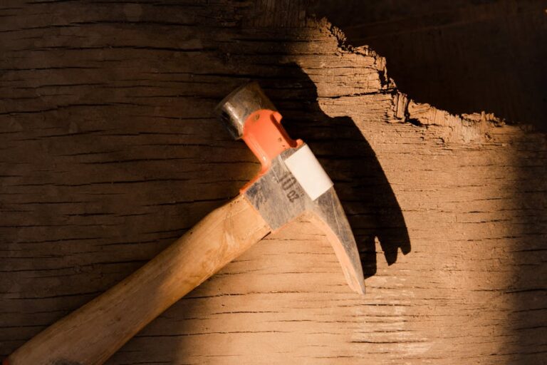 A hammer rests on a rugged, sunlit wooden surface, symbolizing repair and construction.