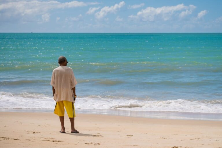 A man contemplates the serene ocean view at Porto Seguro Beach in Brazil under a clear blue sky.
