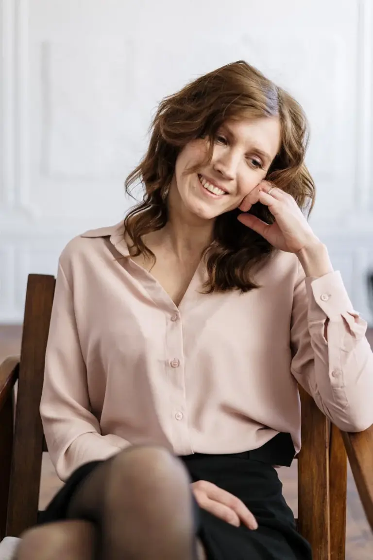 A relaxed woman with curly hair smiling while sitting in an armchair indoors. Perfect for mental health and wellness themes.