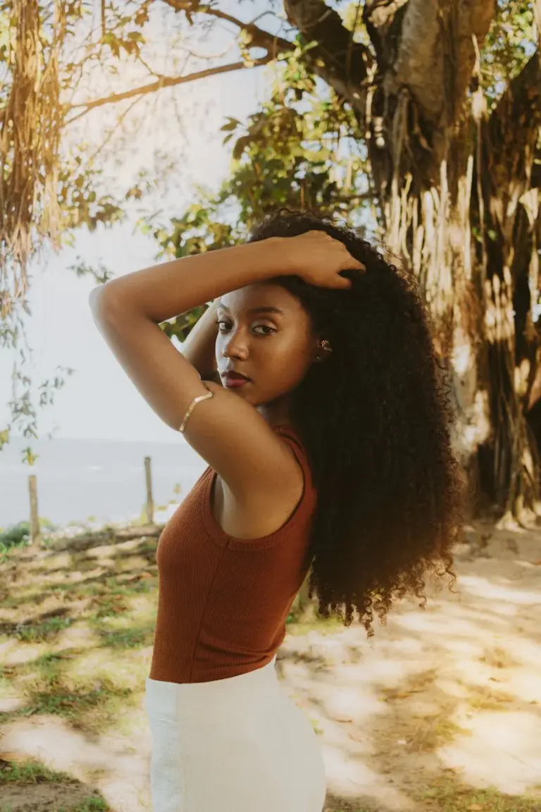 Elegant portrait of a woman with curly hair posing under a tree in Porto Seguro, Brazil.