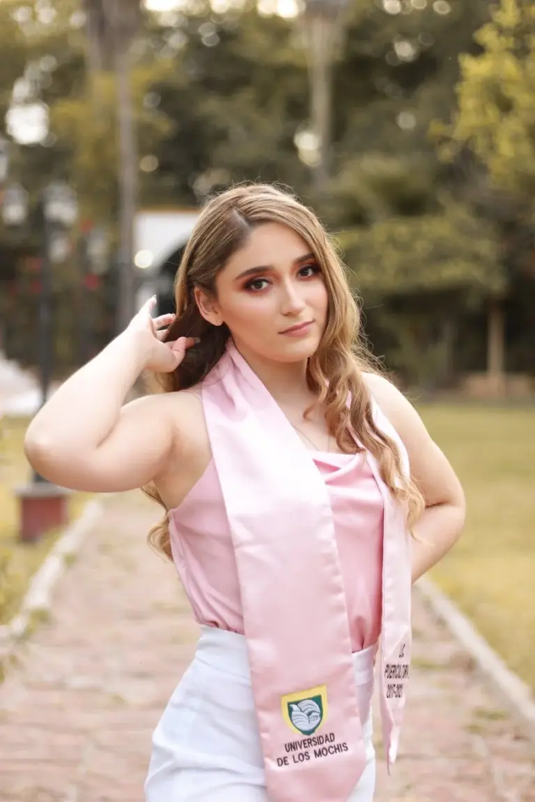 A young woman outdoors wearing a pink graduation stole from Universidad de Los Mochis.