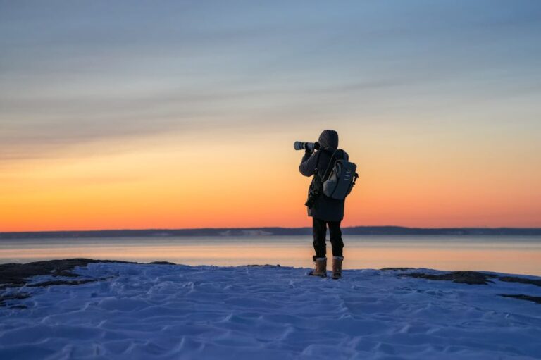A solitary photographer capturing the stunning winter sunset by a snowy lakeside.