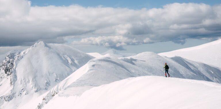 A lone skier traverses snow-covered peaks under a cloudy sky, showcasing winter's beauty.