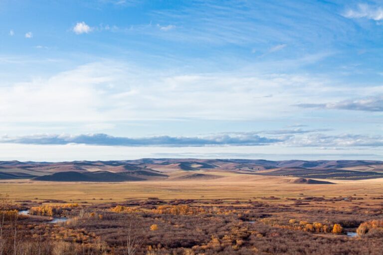 Scenic aerial view showcasing the vast autumn landscape and open fields of Inner Mongolia under a blue sky.